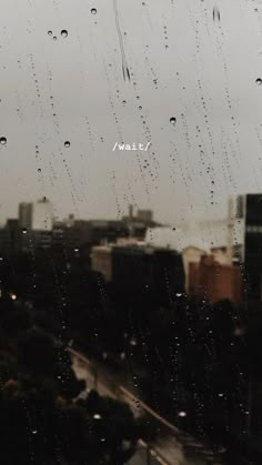 raindrops are falling down on the window pane in front of a cityscape