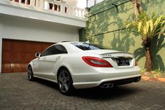 a white mercedes cls parked in front of a green building with palm trees on the side