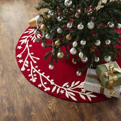 a christmas tree with presents under it on a red rug next to a wooden floor