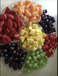 an assortment of fruits arranged in a circle on a plate with grapes, strawberries, and oranges