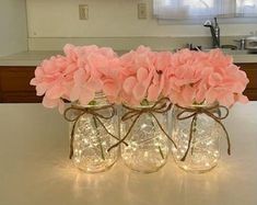 three mason jars filled with pink flowers sitting on top of a counter