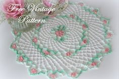 a crocheted doily with pink roses on it and a glass vase next to it