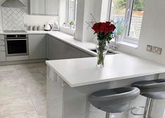 a white kitchen with two stools and a vase filled with flowers on the counter