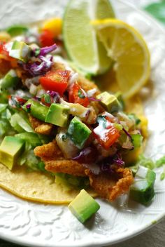 fish tacos with avocado, tomatoes and cilantro on a white plate