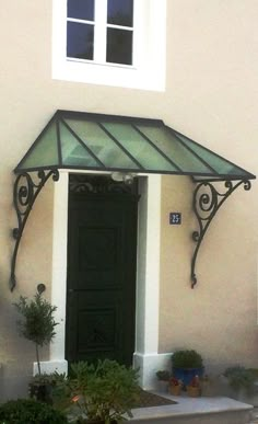 a black door with a green awning over it and potted plants in front