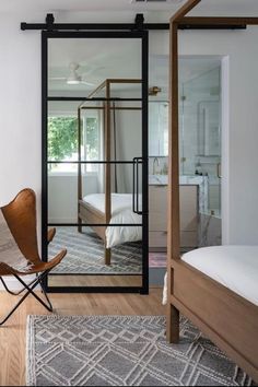 a bedroom with a bed, chair and glass door leading to another room that has a large mirror on the wall