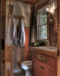 a bathroom with a toilet, sink and mirror in it's corner next to a window