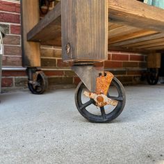 an old wooden cart with wheels on the ground next to a brick wall and floor