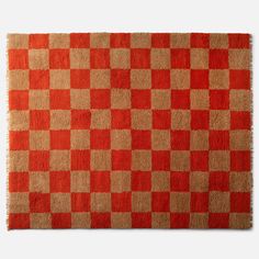 an orange and beige checkered rug with fringes on the bottom, in front of a white background