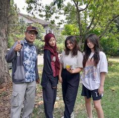 four people standing in front of a tree giving the thumbs up