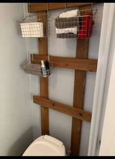 a toilet in a small bathroom with wooden shelves above the toilet and towel racks on the wall