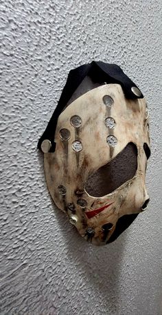 a mask hanging on the side of a wall with rivets and holes in it