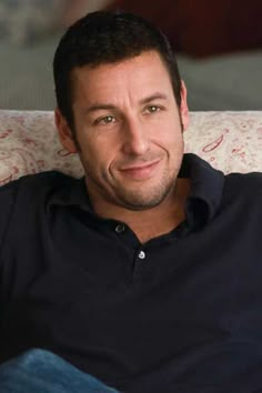 a black and white photo of a man sitting on a couch smiling at the camera