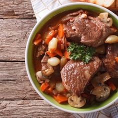 a bowl filled with meat and vegetables on top of a table next to some bread