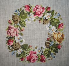 a cross stitched wreath with roses and leaves on the front, surrounded by smaller flowers