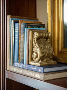 books are stacked on top of each other in front of a gold framed mirror and ornate bookend