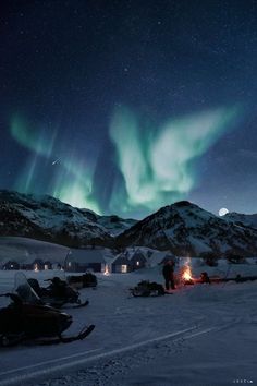 the northern lights shine brightly in the sky above snow covered mountains and campfires