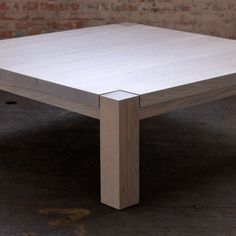 a square wooden table sitting on top of a hard wood floor next to a brick wall