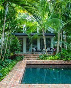 an outdoor pool surrounded by palm trees and other greenery in front of a house