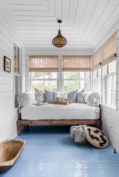 a room with blue floors and white walls, including a bed in the corner between two windows