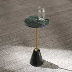 a small black table with a glass on top and a gold leg in the middle