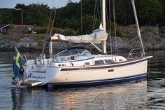 a sailboat in the water next to a shore with trees and rocks behind it