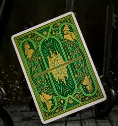 a green and gold playing card sitting on top of a wooden table in front of a black background