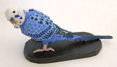 a beaded blue bird sitting on top of a black piece of wood with it's head turned to the side