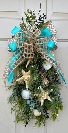 a wreath with starfishs, seashells and greenery hanging on a door