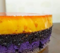 a cake with purple and yellow frosting sitting on top of a wooden table next to a cup