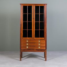 an old wooden cabinet with glass doors on the front and drawers in the back, against a gray wall