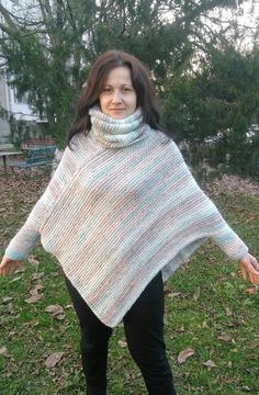 a woman standing in the grass wearing a knitted ponchy with her hands out