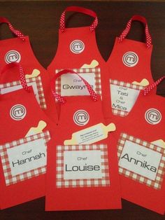 six red aprons with name tags attached to them