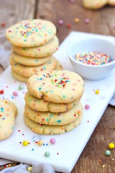 several cookies with sprinkles on a white plate next to a small bowl