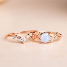 two gold rings with white opal and diamonds on them sitting on a beige surface