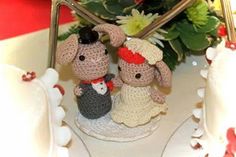 two small crocheted figurines sitting on top of a white plate next to flowers