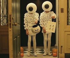 two children dressed up in white holding pumpkins and looking at each other through an open door