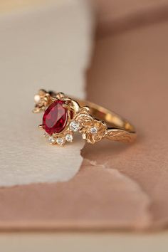 a gold ring with a red stone surrounded by small white diamonds on a piece of paper