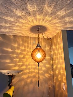 a lamp hanging from the ceiling in front of a wall with light shining on it