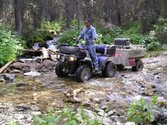 a man riding on the back of an atv across a stream in a wooded area