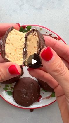 two hands holding chocolate covered desserts on a white and red plate with green leaves