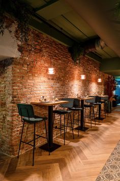 an empty restaurant with wooden floors and brick walls, along with green velvet bar stools