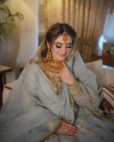 a woman in a blue and gold bridal outfit sitting on a couch with her hands under her chin