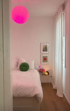 a white bed sitting under a pink light in a bedroom