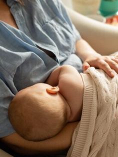 a woman holding a baby wrapped in a blanket on top of a couch next to a bowl