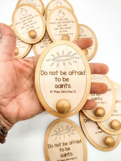 a hand holding some wooden magnets with words on them that say do not be afraid to be saints