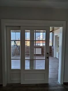 an empty room with two double doors leading to the balcony and deck area in the background