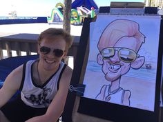 a man sitting in front of a drawing on a easel next to a beach