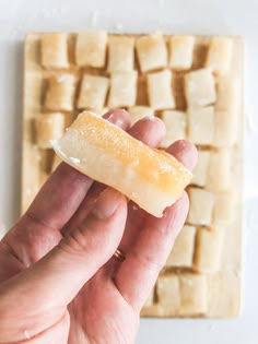 a hand holding a piece of food in front of a white surface with squares on it