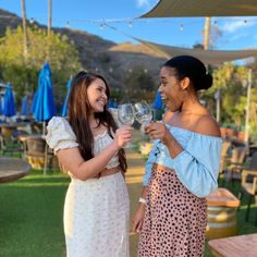 two young women standing next to each other holding wine glasses in their hands and laughing